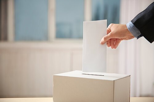 Hand wirft einen Wahlumschlag in Wahlurne
