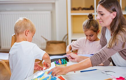 The teacher helping a child and they are working together making some paper crafts. Developing Fine motor skills for toddlers and preschoolers